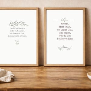 May include: Two framed prints with German text, featuring botanical illustrations and prayers. The prints are in wooden frames, displayed on a wooden table. A lit candle and a bread loaf are also visible.