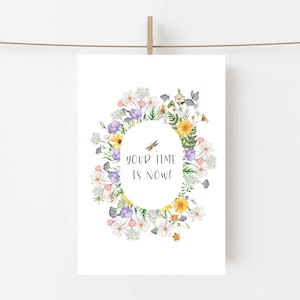 May include: A white card with a floral design and the text "your time is now!". The oval-shaped design features a variety of colorful flowers, including yellow, purple, and white blooms, with a dragonfly illustration.