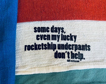Cotton towel with printed quotation: "Some days, even my lucky rocketship underpants don't help." Choose blue, red, white, or sea foam green