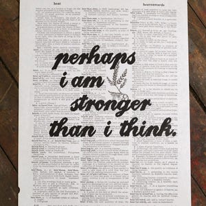 May include: Printed on aged paper, this artwork features the words "perhaps I am stronger than I think" in bold, black lettering. A sprig of leaves accents the text, evoking themes of resilience and self-belief.