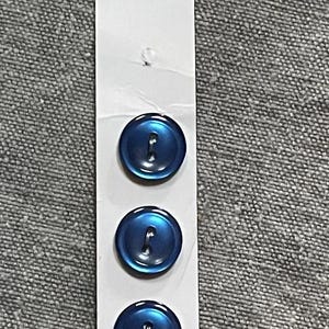 May include: A vertical white card featuring four round, metallic blue buttons with two holes each. The card displays the text Slimline at the top and the word WASHABLE at the bottom. The buttons are arranged in a single column on the card.