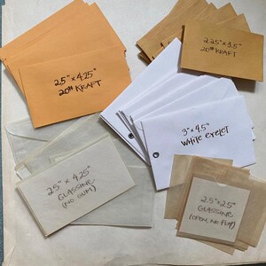 May include: A collection of small envelopes including tan kraft envelopes labeled 2.5" x 4.25" 20# KRAFT and 2.25" x 3.5" 20# KRAFT, white eyelet envelopes labeled 3" x 4.5" WHITE EYELET, and translucent glassine envelopes labeled 2.5" x 4.25" GLASSINE (NO GUM) and 2.5" x 2.5" GLASSINE (OPEN, NO FLAP).