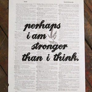 May include: Printed artwork on aged paper features the words "perhaps I am stronger than I think" in bold black letters. The text is overlaid on a dictionary page with botanical illustrations.