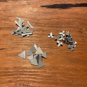 May include: A collection of small metal hardware components consisting of three distinct groups: a pile of elongated pointed metal pieces, a cluster of small Y-shaped metal fasteners, and a group of flat, silver-coloured triangular metal shapes.
