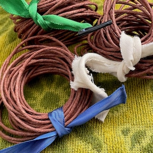 May include: Coiled brown twine bundles tied with green, white, and blue ribbons. The twine is tightly wound, and the ribbons are neatly knotted. The image is a close-up shot, highlighting the texture and color variations of the materials.