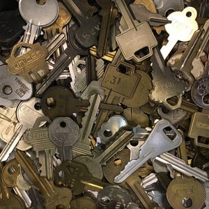 A pile of various metallic keys, likely composed of brass and steel, with inscriptions such as '31' and 'UBL' visible.