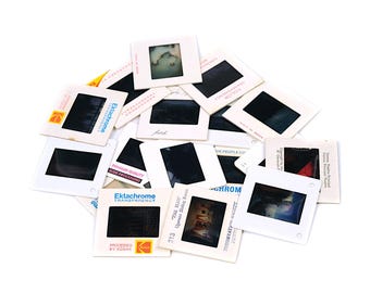 Può includere: Una collezione di diapositive fotografiche quadrate con telai in cartone bianco. Ogni diapositiva presenta un fotogramma centrale rettangolare, alcune con testo visibile tra cui Ektachrome Transparency, loghi Kodak e note scritte a mano.