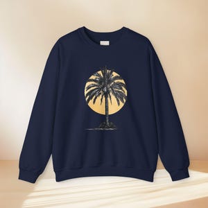 Könnte beinhalten: Ein marineblaues Sweatshirt mit Rundhalsausschnitt und einem mittigen Grafikdruck, der die schwarze Silhouette einer Palme vor einem großen, hellgelben Kreis zeigt. Das Kleidungsstück hat lange Ärmel und einen gerippten Halsausschnitt.