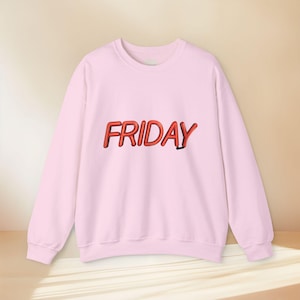 Può includere: Una felpa girocollo rosa chiaro con la parola FRIDAY stampata sul petto in un audace carattere rosso tridimensionale che imita l'aspetto di un'insegna al neon luminosa con un sottile effetto di ombra portata nera.