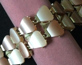 May include: A vintage bracelet with a gold-tone metal setting and triangular, iridescent, light-colored stones. The bracelet is displayed on a pink velvet surface against a black background. The stones vary in color from white to light brown.