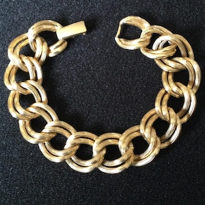 May include: Gold-toned bracelet featuring a series of interlocking, double-loop chain links. The bracelet is shown against a dark background, with the clasp open. The jewelry piece has a polished finish.