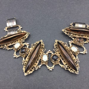 May include: A gold and silver bracelet with brown and white glass stones. The bracelet has a filigree design and is made of metal.