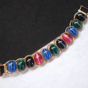 May include: A gold bracelet with oval-shaped stones in shades of blue, green, black, and pink. The stones have a striped pattern.