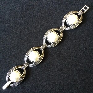 Peut inclure: Bracelet argent&eacute; compos&eacute; de quatre maillons ovales, chacun avec un grand centre rond blanc semblable &agrave; une perle. Les maillons sont reli&eacute;s par de petits connecteurs d&eacute;coratifs. Le bracelet a une fermeture &agrave; fermoir.