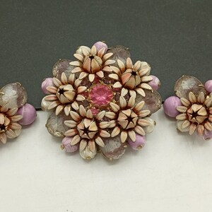 May include: A set of vintage jewelry featuring a large brooch and two earrings. The brooch and earrings are made of white and pink flower-shaped beads with a pink rhinestone in the center of the brooch.