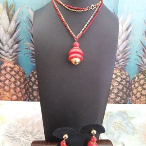 May include: A red and gold necklace with a layered chain and a pendant shaped like a stack of red circles. Matching red and gold earrings with a similar design.