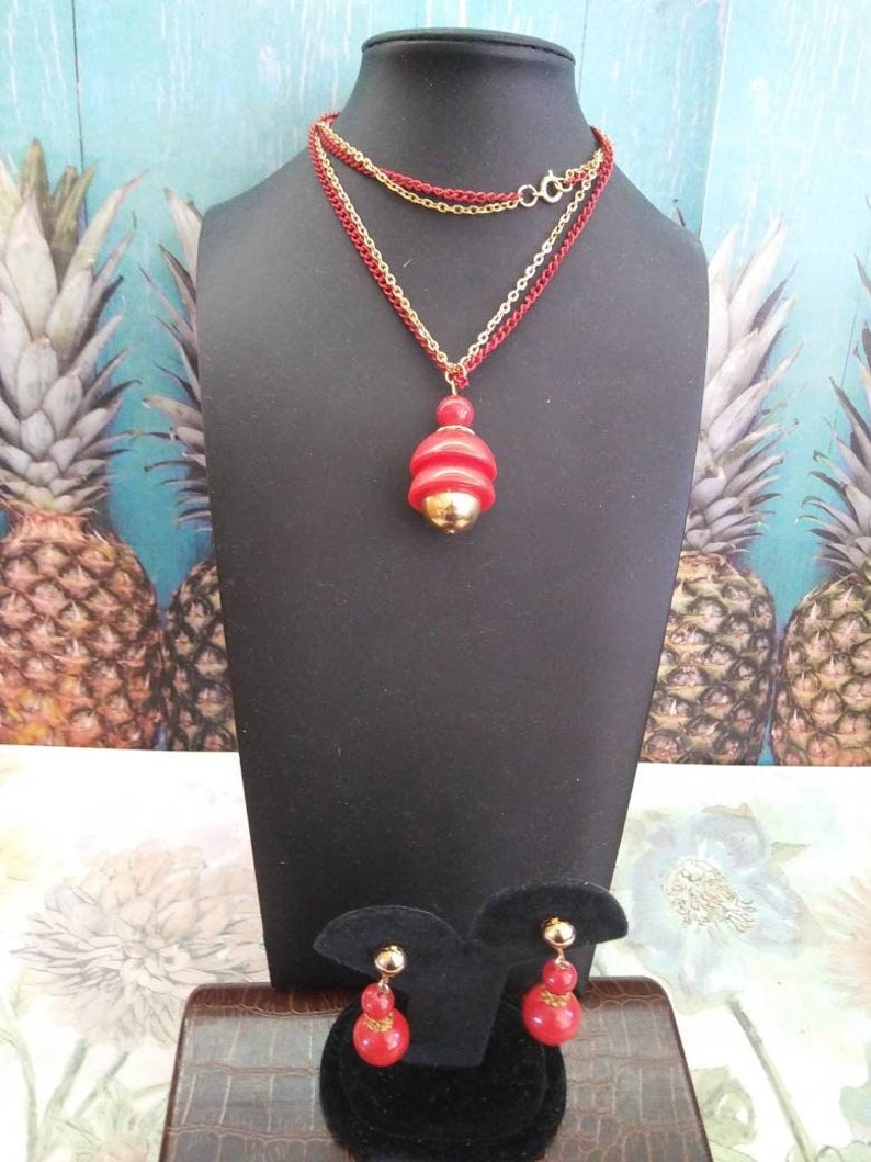 May include: A red and gold necklace with a layered chain and a pendant shaped like a stack of red circles. Matching red and gold earrings with a similar design.