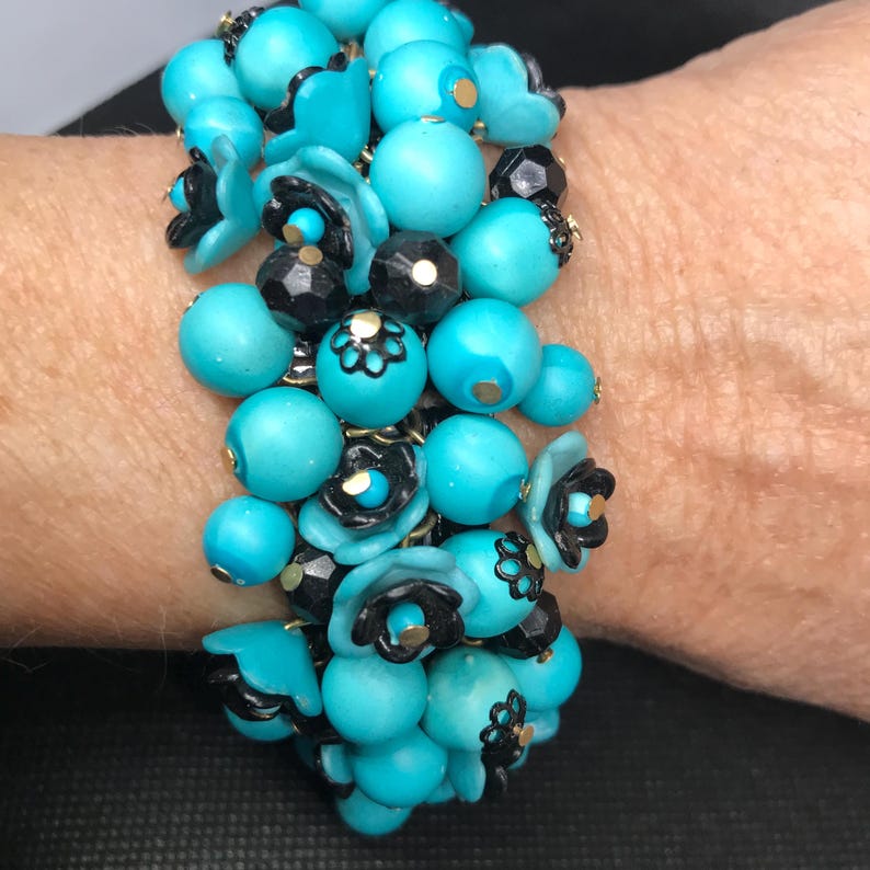 May include: A turquoise and black beaded bracelet with flower accents. The bracelet is made of round beads and small flower-shaped beads.