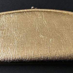 Könnte beinhalten: Eine goldfarbene Clutch mit einer strukturierten, genarbten Lederoberfläche. Die Clutch hat eine geschwungene Form und einen Verschluss mit einem Druckknopf.