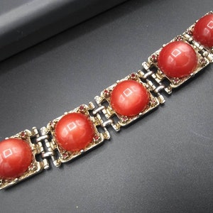 May include: A vintage bracelet featuring five large, round, coral-colored cabochons set in gold-toned metal squares. The squares are connected by a silver-toned chain. Small red rhinestones accent the edges of the cabochon settings.