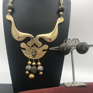 May include: A gold necklace with a geometric design and black and gold beads. The necklace is on a black stand. A pair of black and gold earrings are on a silver stand with a heart-shaped design.