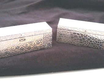 May include: Two silver decorative boxes with intricate floral and textured patterns. The boxes have a hinged lid and are closed.