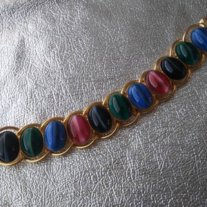 May include: A gold chain bracelet with oval-shaped gemstones in shades of blue, green, black, and pink.