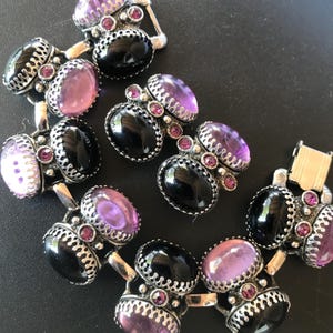 Peut inclure: Ensemble de boutons de manchette argent&eacute;s vintage avec des pierres pr&eacute;cieuses ovales noires et violettes. Chaque bouton de manchette pr&eacute;sente une bordure argent&eacute;e d&eacute;corative et de petites pierres roses. Les boutons de manchette sont dispos&eacute;s sur une surface sombre.