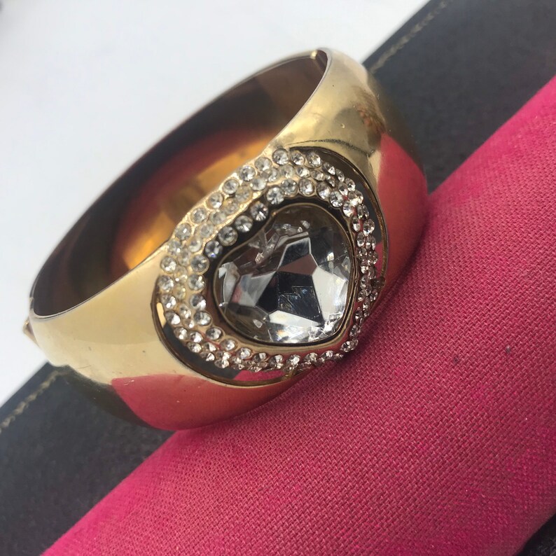 Puede incluir: Un brazalete de oro con un gran coraz&oacute;n de cristal transparente engastado en un marco en forma de coraz&oacute;n de cristales m&aacute;s peque&ntilde;os.