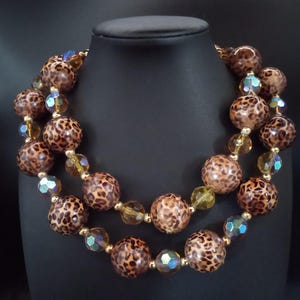 以下が含まれることがあります： レオパード柄の大きな丸いビーズが特徴の2連ネックレス。ゴールドとイリデッセントブルーグリーンの小さなファセットビーズも含まれています。黒いマネキンに飾られています。目を引くジュエリーです。