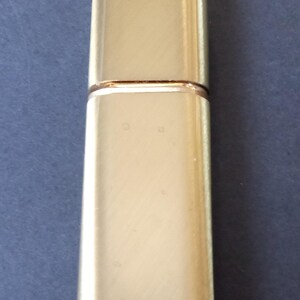 May include: A gold metal perfume bottle with a rectangular shape.