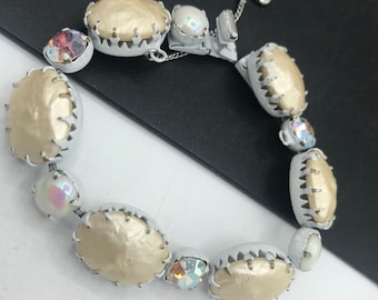 May include: A white and cream pearl bracelet with a silver clasp and iridescent rhinestones.