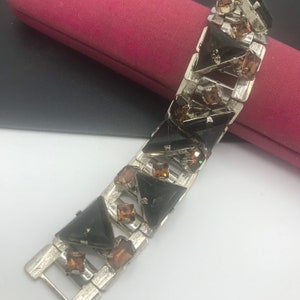 May include: A silver bracelet with a chain link design features alternating black and brown triangular rhinestones.