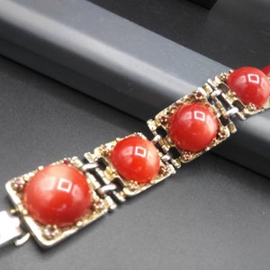 May include: A vintage bracelet featuring large, round, red cabochon stones set in gold-toned metal frames. The bracelet has a silver-colored clasp and is accented with small, reddish-brown stones. The design is geometric and classic.