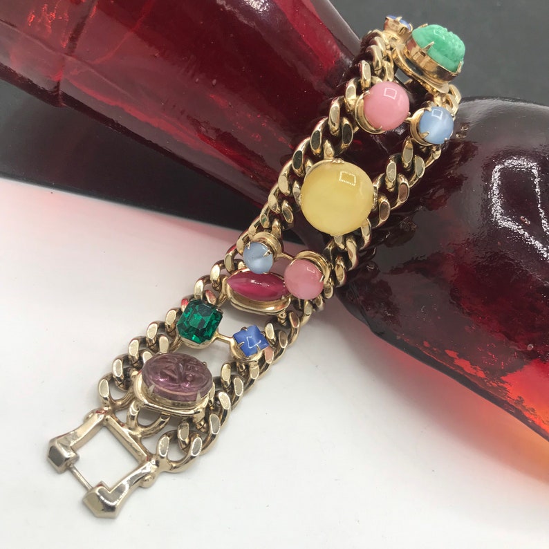 May include: A gold chain bracelet with colorful glass stones. The stones are in various shapes and sizes, including round, oval, and square. The bracelet has a clasp closure.
