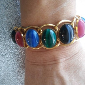 May include: A gold chain bracelet with oval-shaped gemstones in shades of red, blue, green, and black.