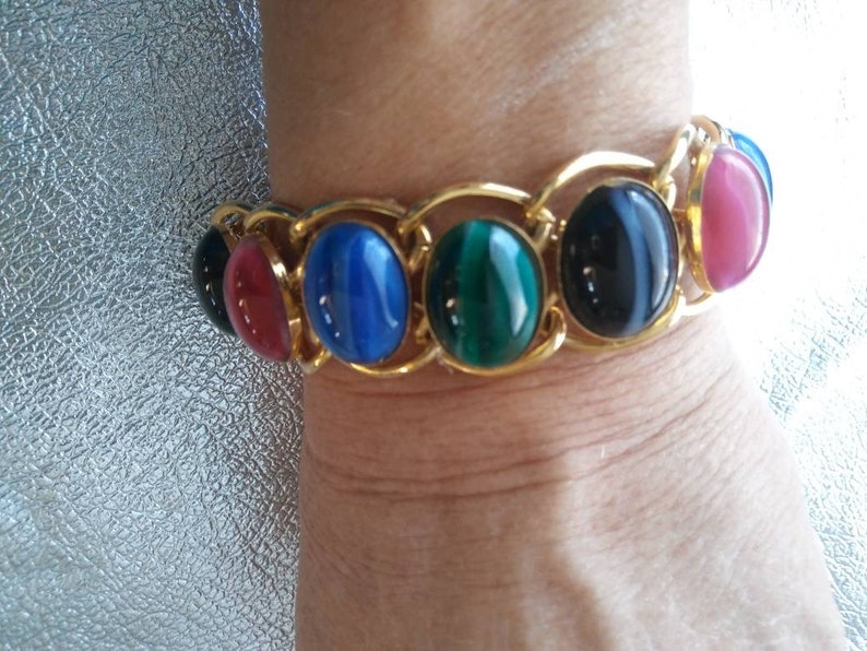 May include: A gold chain bracelet with oval-shaped gemstones in shades of red, blue, green, and black.