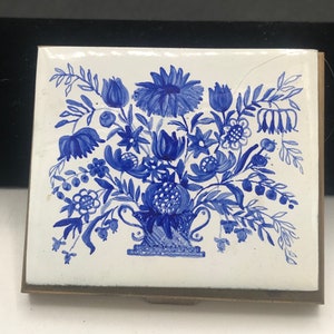 May include: A vintage blue and white floral design on a brass matchbox. The floral design is in a blue and white color scheme and features a variety of flowers and leaves.