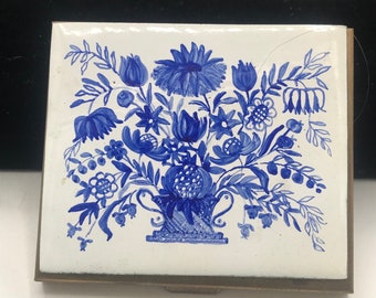 May include: A vintage blue and white floral design on a brass matchbox. The floral design is in a blue and white color scheme and features a variety of flowers and leaves.