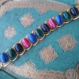May include: A gold chain bracelet with oval-shaped gemstones in shades of blue, green, and pink. The gemstones have a cat's eye effect.