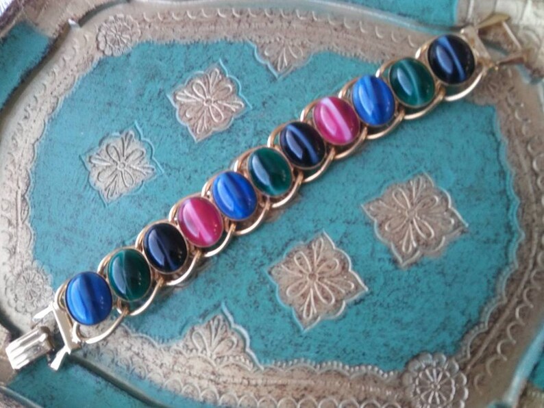 May include: A gold chain bracelet with oval-shaped gemstones in shades of blue, green, and pink. The gemstones have a cat's eye effect.