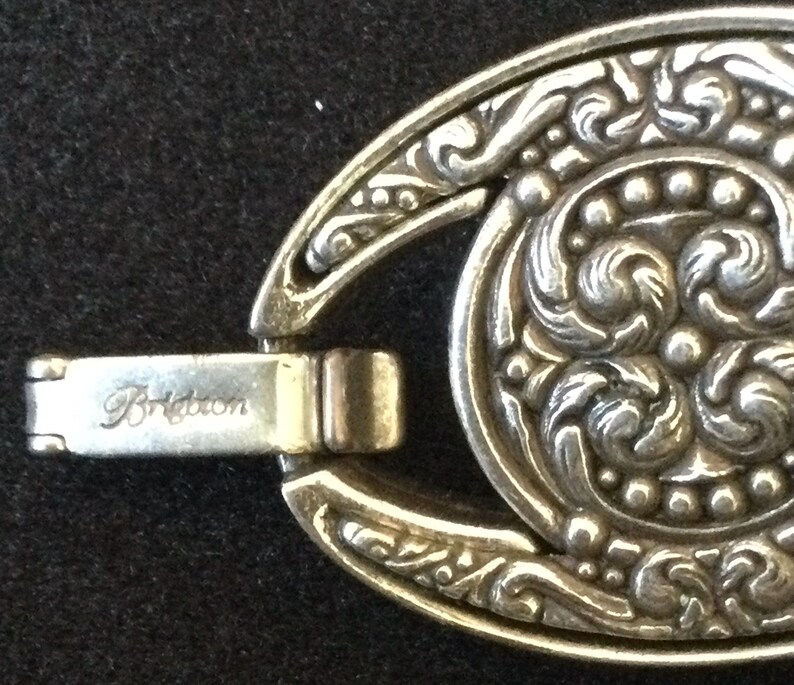 Peut inclure: Gros plan sur un fermoir de bracelet Brighton argent&eacute;. Le fermoir pr&eacute;sente un design ovale avec des motifs floraux et volutes complexes. Le mot "Brighton" est grav&eacute; sur le fermoir.