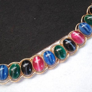 May include: A gold chain bracelet with oval-shaped gemstones in shades of blue, green, black, and pink. The gemstones have a striated pattern.