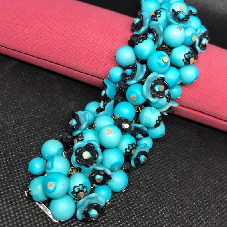May include: A turquoise and black beaded bracelet with flower accents. The bracelet is made of round beads and small flower-shaped beads.