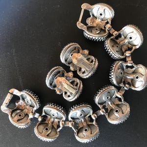 Peut inclure: Boucles d'oreilles &agrave; clip et bracelet assorti de couleur argent&eacute;e vintage. Les bijoux pr&eacute;sentent un design d&eacute;taill&eacute; avec de petits accents sombres sur les bords. Les pi&egrave;ces sont dispos&eacute;es sur une surface sombre, mettant en valeur leur savoir-faire.