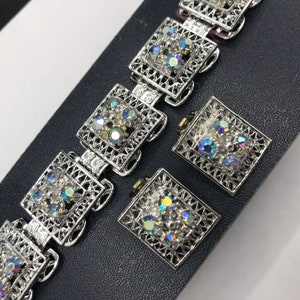 Pu&ograve; includere: Un braccialetto d'argento e un paio di orecchini con un design a filigrana e strass iridescenti.