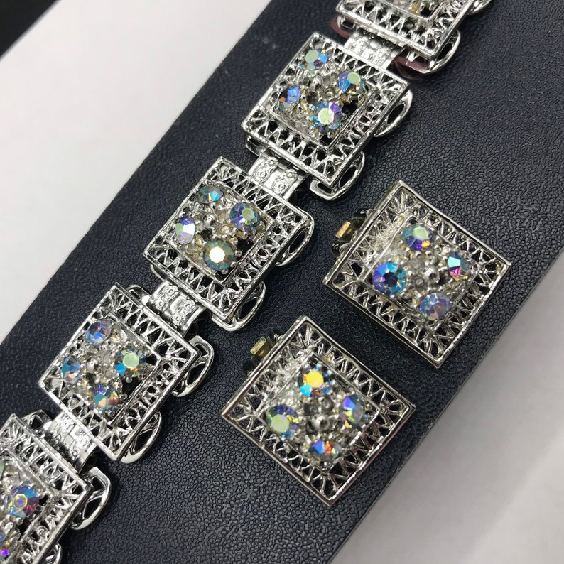 Pu&ograve; includere: Un braccialetto d'argento e un paio di orecchini con un design a filigrana e strass iridescenti.