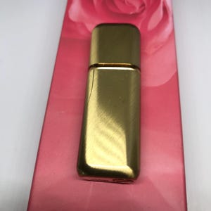 May include: A gold-colored metal perfume bottle with a brushed finish. The bottle is rectangular and has a rounded top.