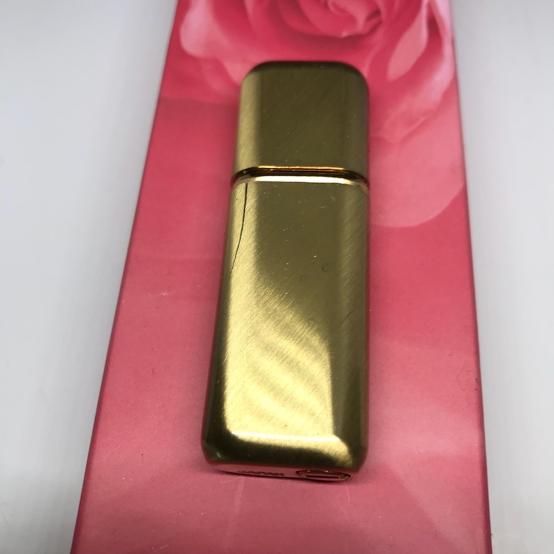 May include: A gold-colored metal perfume bottle with a brushed finish. The bottle is rectangular and has a rounded top.