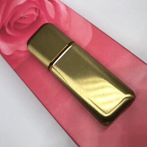 May include: A gold metal perfume bottle with a brushed finish. The bottle is rectangular with rounded edges and has a thin gold band around the middle.
